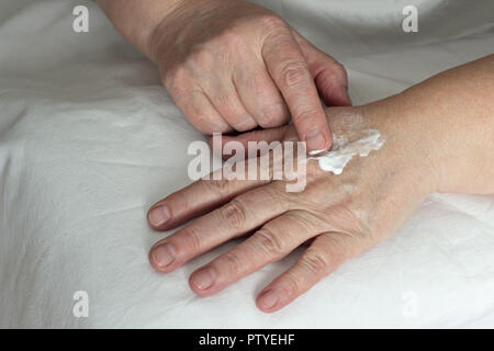 Donna anziana sfregamento Crema mani, sfondo bianco, close-up Foto Stock