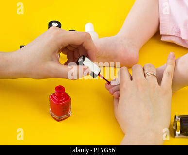 Una madre dipinge il suo toenails con la sua piccola figlia, uno sfondo giallo, close-up Foto Stock