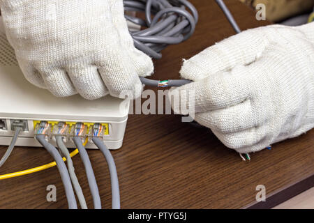 Un uomo in guanti contiene un cavo di rete, un modem, un close-up Foto Stock