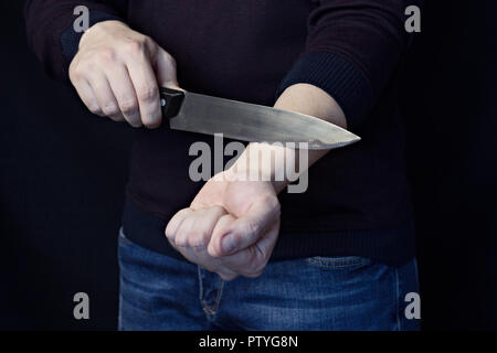 Un uomo è il taglio di una vena sulla sua mano, uno sfondo nero Foto Stock