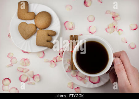 Lettera d'amore da un cookie, la mano che regge una tazza di caffè su sfondo bianco Foto Stock