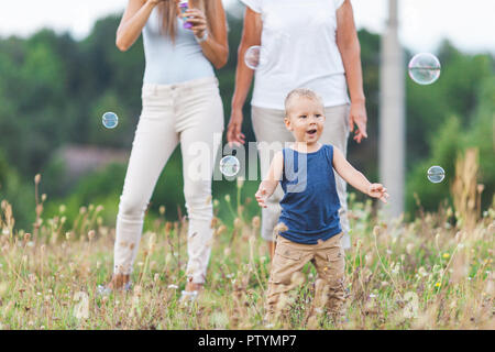 Bambino felice con la famiglia avente un grande tempo a soffiare bolle all'aperto Foto Stock