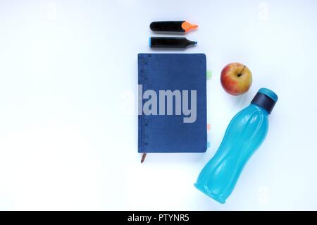 Studio roba. Sfondo dell'istruzione. Articoli di cancelleria. Gli aspetti dell'istruzione. Marcatori, Apple, bottiglia di colore blu e il portatile sul tavolo. Foto Stock