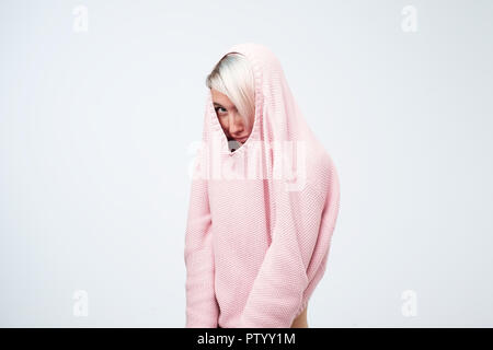 Una bella ragazza caucasica con una fobia sociale nasconde il suo volto in un maglione. Lei si guarda intorno spaventati Foto Stock