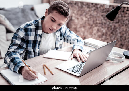 Attento studente rendendo note mentre si fanno i compiti Foto Stock