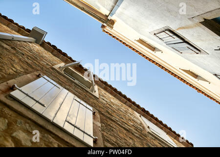 Facciate delle vecchie case di pietra con finestre con persiane sul cielo azzurro sfondo in Budva in Montenegro. Sole splende su di essi. Orizzontale. Foto Stock