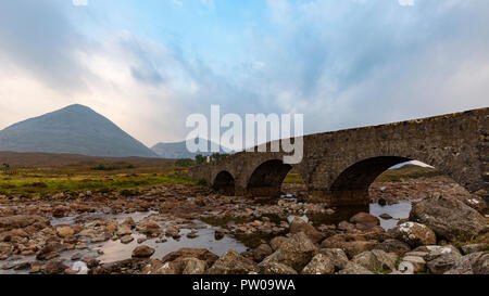 Il vecchio ponte Sligachan con Nero montagne Cuillin in background e basse nuvole pensili, Isola di Skye in Scozia Foto Stock