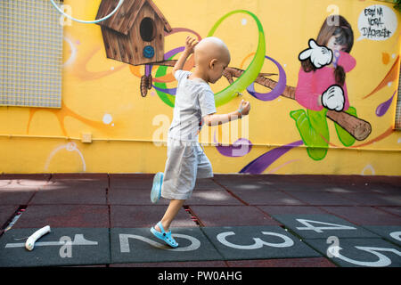 Ragazzo giovane con il cancro a giocare sul campo giochi. Foto Stock