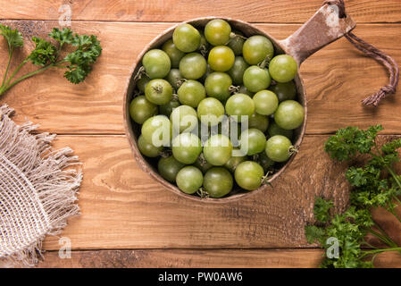 Vista da sopra su verdi maturi delle varietà rotondo piccolo pomodori ciliegia nel ciclo naturale sulla ciotola di legno a trama la superficie del tavolo verde con foglie di prezzemolo