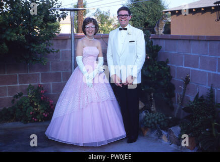 1962, America, andando a prom.....un giovane uomo che indossa uno smoking bianco e e una giovane donna che indossa una lunga frilly abito rosa di stare in piedi insieme a un'immagine prima di frequentare la PROM, un importante e tradizionale fine del termine di danza e un evento sociale per noi studenti di scuola superiore. Negli anni cinquanta e sessanta, PROM è stato più di un paio di evento, dove un ragazzo chiede ad una ragazza per essere la sua data e alla scorta di lei dopo il prelievo di lei fino a casa sua e con un sacco di foto scattata! Foto Stock