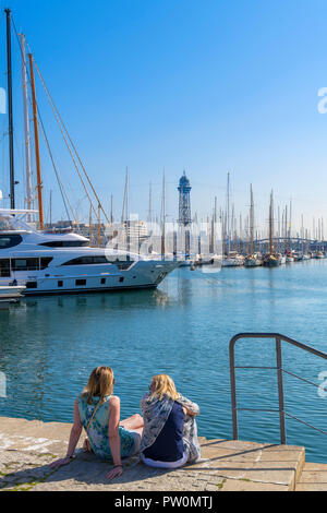 Due giovani donne seduti sulla banchina nel Port Vell (Vecchio porto), Moll de Bosch mi Alsina, Barcellona, Spagna Foto Stock