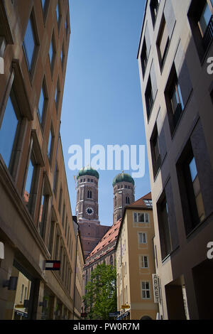 Vista della cattedrale Frauenkirche di Monaco di Baviera, Germania, da un lato della strada. Le due torri con l'orologio della chiesa sono visibili e il colpo è incorniciato da Foto Stock