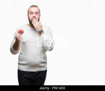 Giovani caucasici uomo parigamba mangiare ciambella dolce su sfondo isolato coprono la bocca con la mano sconvolto con vergogna per errore, espressione di paura, scar Foto Stock