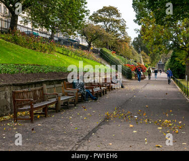 I giardini di Princes Street, Edimburgo, Scozia, Regno Unito, 12 ottobre 2018. Meteo REGNO UNITO: Red color acero e in legno panchine lungo il sentiero in autunno Foto Stock