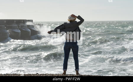 Brighton Regno Unito XII Ottobre 2018 - Una donna si blocca sul suo cappello come lei gode di una passeggiata lungo la spiaggia di Brighton questa mattina in alta venti di tempesta Callum spazia su parti della Gran Bretagna oggi Credito: Simon Dack/Alamy Live News Foto Stock