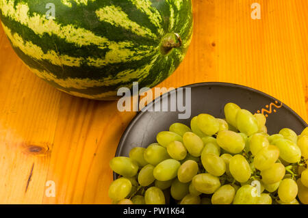 Still Life - un pennello grande di uva verde e anguria in un buio piastra ceramica su uno sfondo di legno Foto Stock