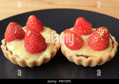 Chiuso una coppia di mini golosa crema pasticcera crostate e rabboccato con fragole fresche e commestibili oro in polvere servito sulla piastra nera Foto Stock