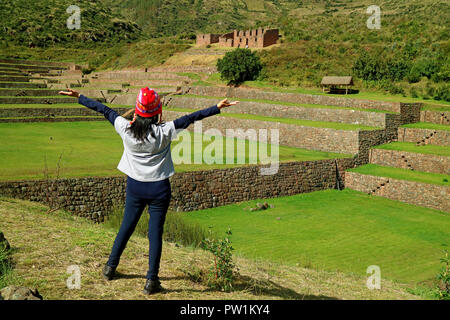 Turista femminile alzando le braccia sensazione impressionato con gradino Inca agricola Rovine di Tipon sito archeologico nella Valle Sacra, Cusco, Perù Foto Stock