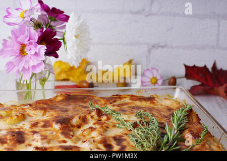 Lasagne con un rametto di rosmarino e timo su una tabella con foglie di autunno e un mazzo di fiori in un vaso Foto Stock