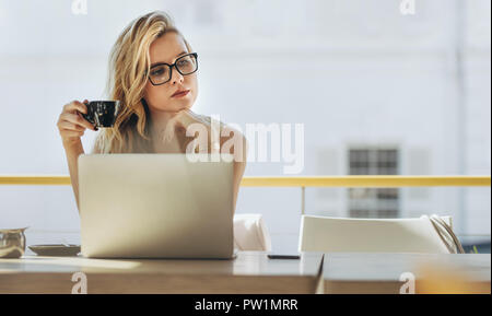 Donna seduta al tavolo del bar con laptop e guardando lontano pensando con tazza di caffè in mano. Imprenditrice avente il caffè e pensando al cafe. Foto Stock