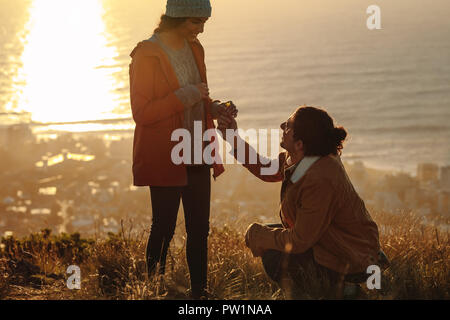 Uomo che fa proposta di matrimonio alla sua ragazza sulla cima della montagna al tramonto. Amanti del mare. coppia in viaggio innamorata in montagna. Foto Stock