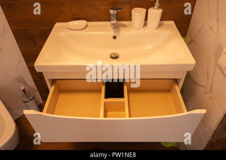 Gli interni moderni del bagno. Il lavello è fatta di bianco guscio massiccia sul tavolo di marmo di colore del legno. Minimalismo e semplicità in un luminoso interno funzionale. Foto Stock