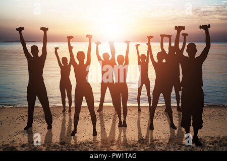 Silhouette di persone che esercitano con manubri sulla spiaggia al tramonto Foto Stock