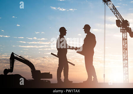 Silhouette di due maschio architetto stringe la mano al sito in costruzione durante il tramonto Foto Stock
