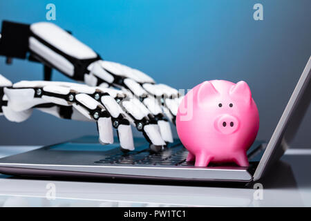 Mano robotica utilizzando laptop con Rosa Piggybank sul tastierino Foto Stock