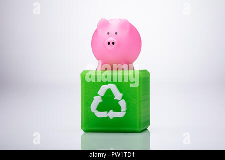 Rosa Piggybank su Blocco cubico con simbolo di riciclaggio su sfondo riflettente Foto Stock