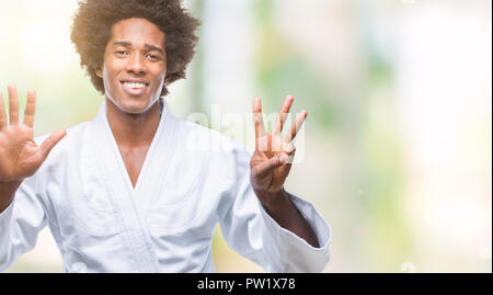 Afro-americano di indossare il kimono di karate più isolato che mostra sfondo e rivolta verso l'alto con le dita in numero otto mentre sorridente fiducioso e contento. Foto Stock