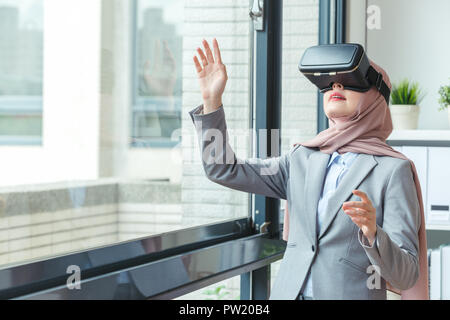 Allegro ufficio musulmano lady indossando la tecnologia VR dispositivo e utilizzando mani toccano simulazione 3D a casa o in ufficio in ufficio. startup concetto di ufficio. Foto Stock