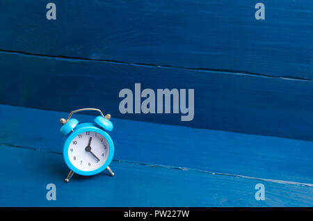 Blue sveglia su un blu sullo sfondo di legno. Il concetto di tempo. Traduzione di ore in inverno o estate. La puntualità e la pianificazione del tempo, Busi Foto Stock