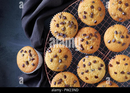 Dodici appena sfornato choco muffin ai chip di raffreddamento sulla maglia di filo su sfondo scuro con biancheria, disposizione piatta Foto Stock