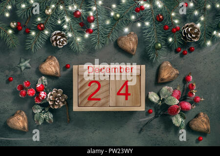 La Vigilia di Natale la data sul calendario, Dicembre 24, con le decorazioni di Natale e la festa di luci su rametti di abete, glassato di bacche rosse e cuori di legno sui gree Foto Stock