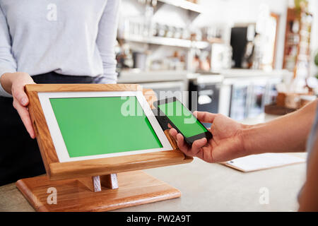 Il cliente effettuando il pagamento tramite smartphone al cafe, close up Foto Stock