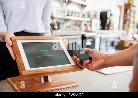 Il cliente effettuando il pagamento tramite smartphone al cafe, close up Foto Stock