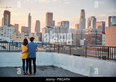 Vista posteriore del giovane sulla terrazza panoramica che affaccia sulla skyline della città al tramonto Foto Stock