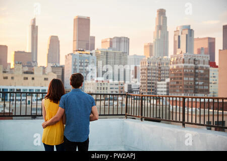 Vista posteriore del giovane sulla terrazza panoramica che affaccia sulla skyline della città al tramonto Foto Stock