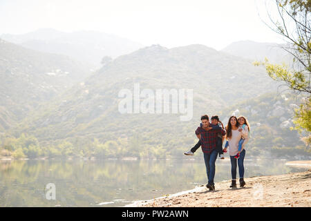 I genitori piggybacking i propri figli da un lago di montagna Foto Stock