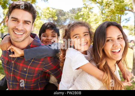 I giovani genitori piggybacking i loro due bambini all'aperto Foto Stock