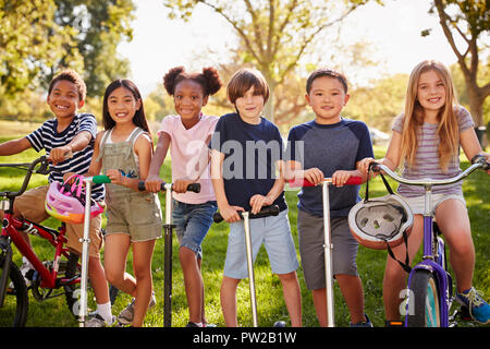 Elementare scuola età i bambini su biciclette e scooter in un parco Foto Stock