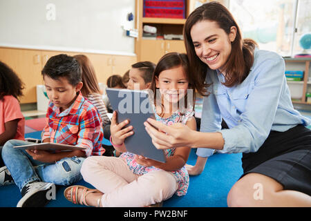 Insegnante e una ragazza in classe elementare utilizzando i computer tablet Foto Stock