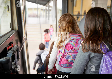 Due ragazze in attesa dietro i loro amici a scendere school bus Foto Stock