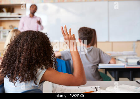 Ragazza alzando la mano per rispondere in una scuola elementare di classe Foto Stock