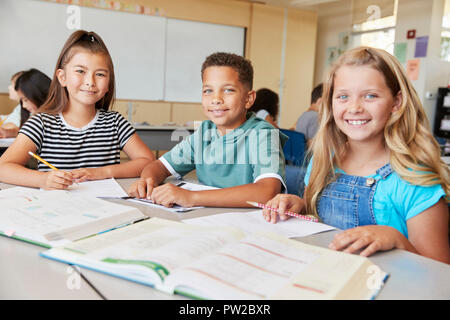 Scuola elementare i ragazzi in classe sorridente alla telecamera, close up Foto Stock