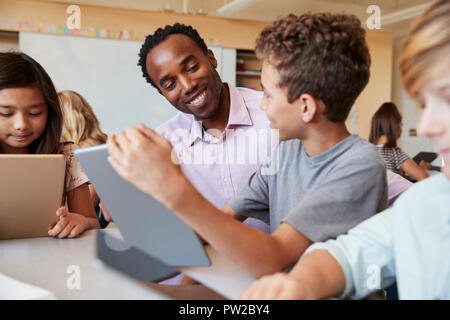 Insegnante utilizzando computer tavoletta alla scrivania con i ragazzi della scuola Foto Stock