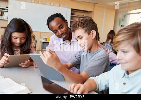 Insegnante di scuola aiuta i ragazzi con i computer tablet in classe Foto Stock