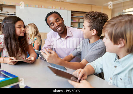 Insegnante di scuola aiuta i ragazzi con i computer tablet in classe Foto Stock