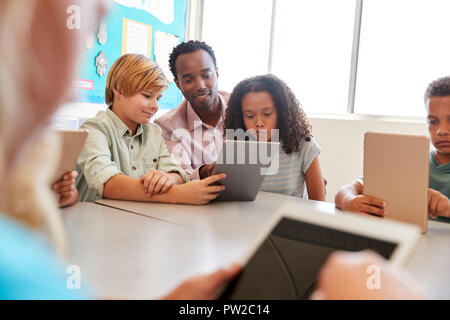 Maestro si siede con giovani figli che utilizzano il computer nella scuola di classe Foto Stock